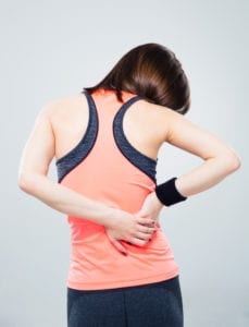 woman in exercise clothes experiencing back pain against solid gray backdrop